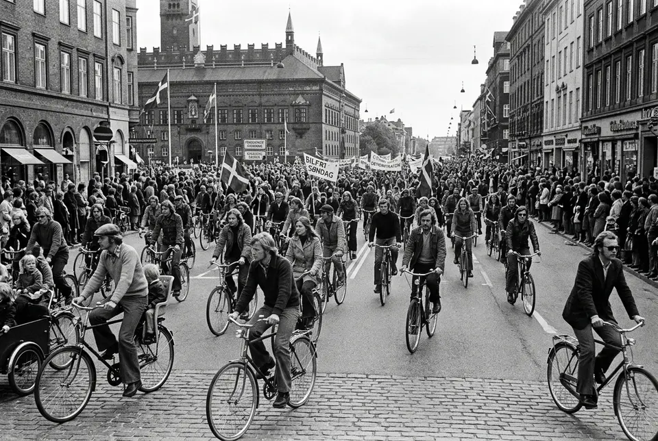black-and-white style street scene of 1970s copenhagen with crowds of cyclists filling a car-free boulevard during a sunday demonstration, illustrating the history of cycling in copenhagen