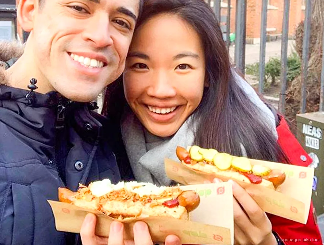 Gids deelt een Deense hotdog proeverij uit tijdens een culinaire fietstour in Kopenhagen
